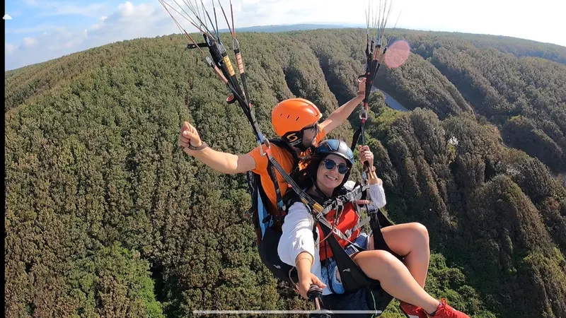 Yeşil orman örtüsü üzerinde pilot ve yolcunun tandem uçuşu