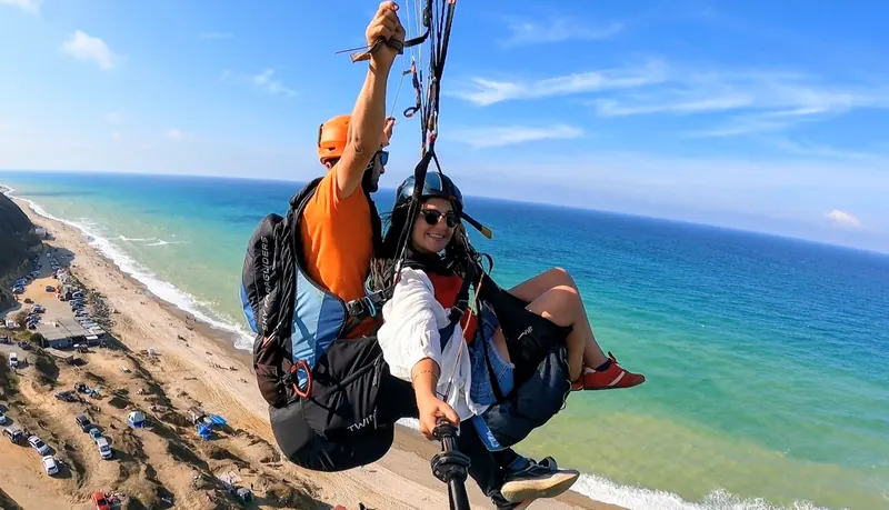Kumlu sahil üzerinde pilot ve yolcunun tandem yamaç paraşütü uçuşu